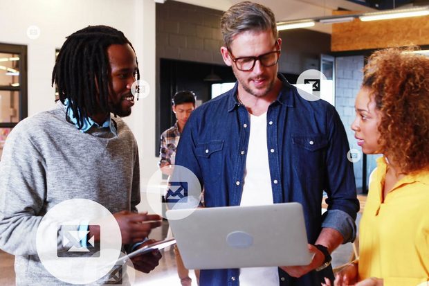 Three coworkers gathered around a laptop in an office, with floating email and document icons.