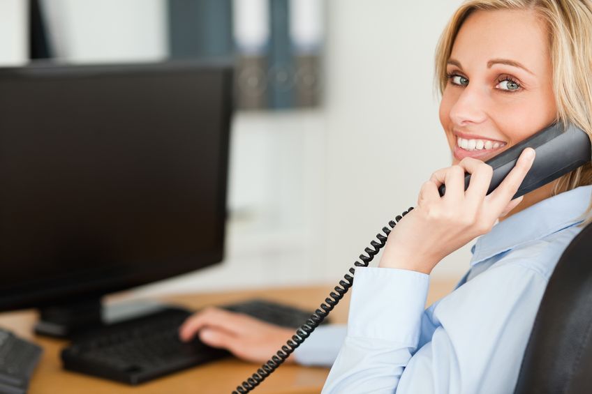 A blonde woman smiling while talking on a business phone