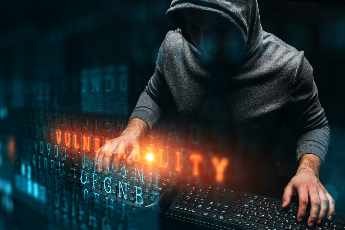 A hacker in a dark hooded sweatshirt overlaid with orange word Vulnerability