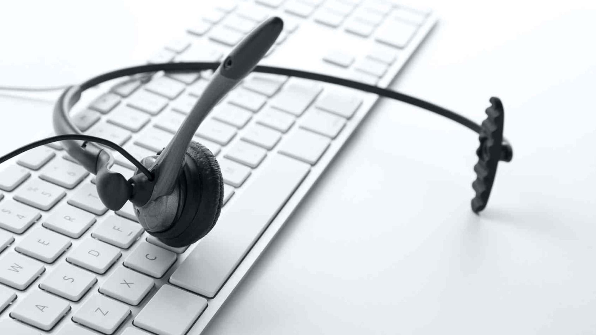 A phone headset, with its mic pointing forward, laying across a white computer keyboard