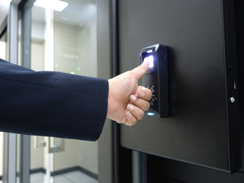 A person in a suit uses a thumbprint scanner on a door to gain access to a secure or restricted area.