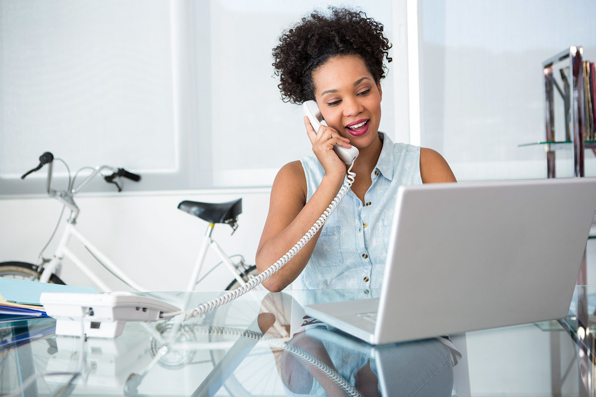 Young casual business woman using telephone and laptop in office.